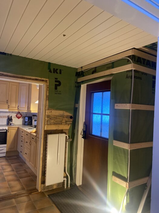 Grön ångbroms installerad på innerväggar och ytterdörr i ett kök med träpanel i taket och beige köksinredning.