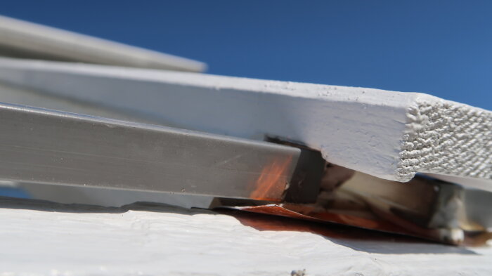 Närbild av spröjs och plastlist på träväxthus med eventuell svag fixering, diskuterar förbättringar av fastsättningen med trälist och tätningslist.