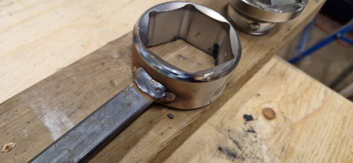 Modifierad 55mm Bacho hylsa med svetsad pinne för kabelgenomföring, liggande på en träyta.