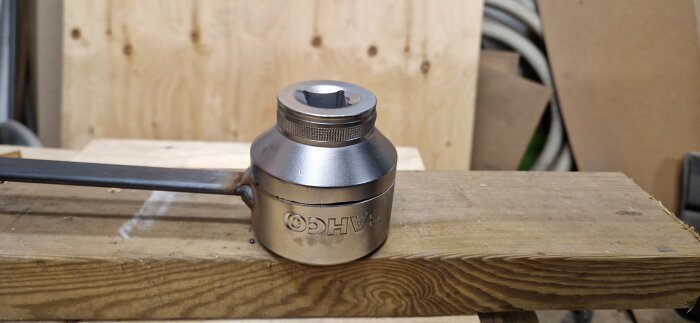 Kraftig, modifierad Bacho 55mm hylsa med svetsad pinne, liggande på en träbit i en verkstadsmiljö.