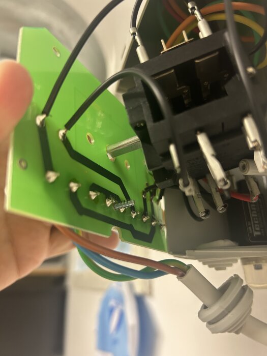 Grönt kretskort med kopplade kablar, nära syn på bak- och ovansidan, svart komponent och färgade trådar synliga.