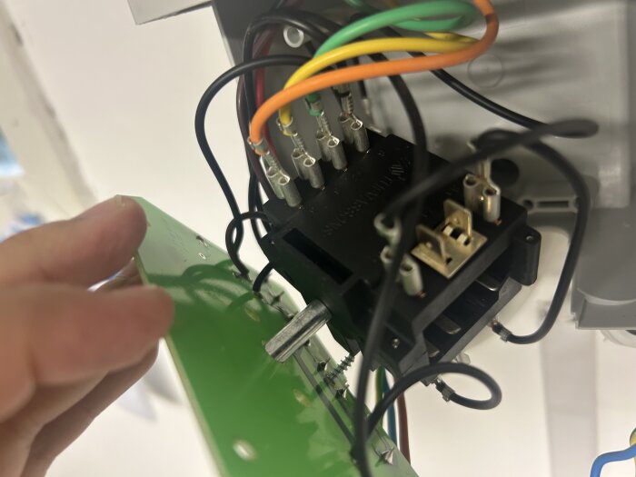 Elektroniskt kretskort som hålls i en hand, anslutet till flera färgade kablar och kontakter inuti en apparat.