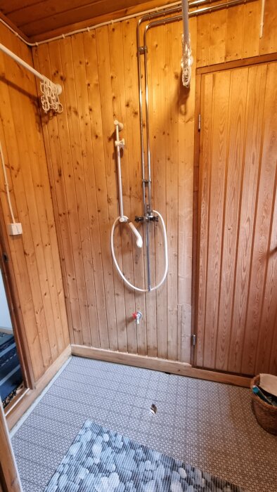 Duschrum i fritidshus med obehandlad träpanel och dusch på väggen; orolig för mögelrisken bakom panelen.