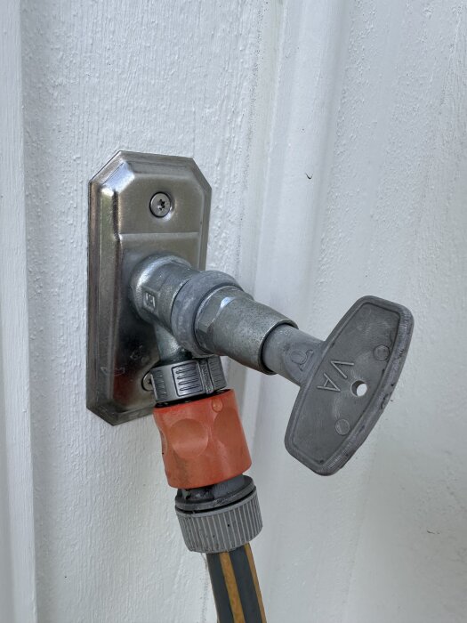 En vattenutkastare med en ansluten gardenaslang monterad på en vit vägg.