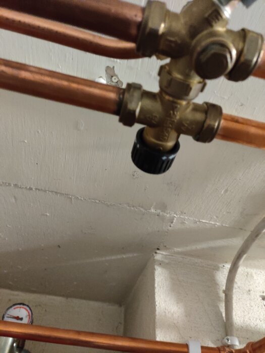 Kopparrör med en ventil i en källare, potentiellt del av ett VVS-system för att stänga av varmvatten i samband med annan röranordning.