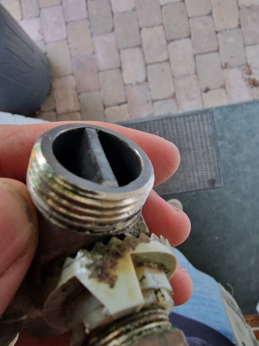 En hand håller en koppling från en radiator utan packning, omgiven av vita och metalliska ytor.