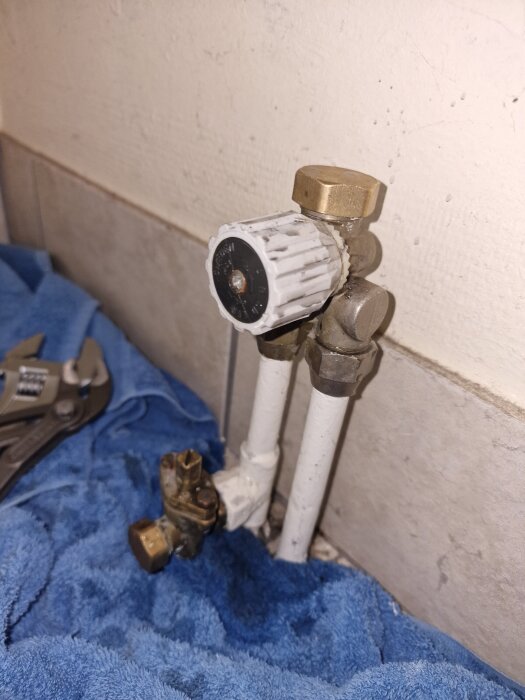 Radiatorventil utan packning, kopplad till två rör ovanför en blå handduk, med skiftnyckel i bakgrunden.