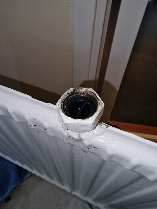 Radiator med avlägsnad koppling, visar frånvaron av packning vid röranslutningen, mot en bakgrund av vitt och beige interiör.