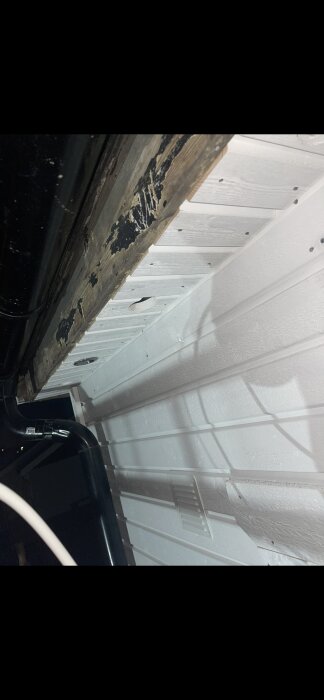 Ventilerad takkonstruktion med synlig isolering och plastplatta, träpanel med ventilationshål och insektsnät, samt svart rör i nederkant.