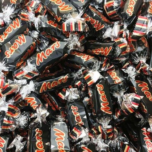 Mars-choklad inslagna i mörka omslag, spridda i en hög.