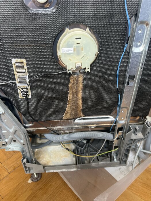 Baksidan av en diskmaskin med kalkbeläggning och synlig sladddragning. Kalkavlagringar syns vid underkant av enhetens insida.