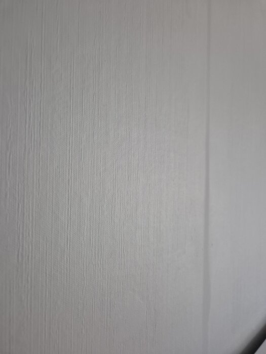 Vit vägg med synliga spackellinjer och randigt tapetmönster i motljus.