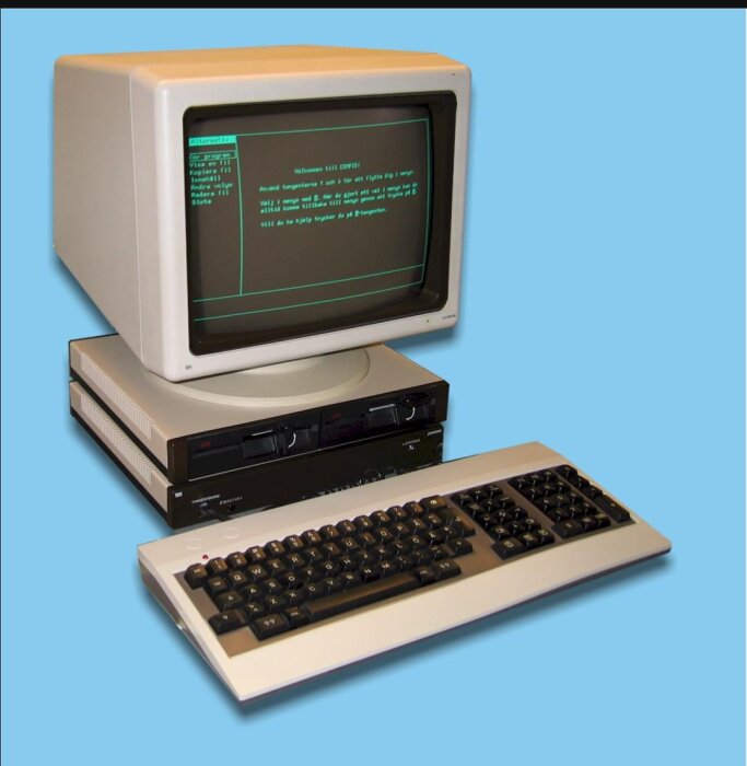 Dator med CRT-skärm, tangentbord och dubbla diskettstationer. Texten på skärmen visar: "Välkommen till COMPIS".