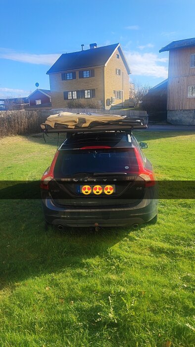 Bil parkerad på gräsmatta med förtält eller markis monterad på takräcket, i bakgrunden syns två hus.