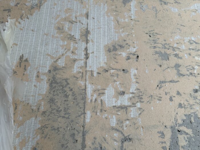 Delvis borttagen tapet på en vägg med synliga rester och fläckar kvar på ytan.
