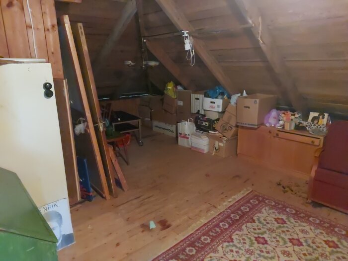 Vind med snedställda takbalkar, kartonger, träpaneler och mattor. Förberedelse för isolering av kallvind i sommarstuga.
