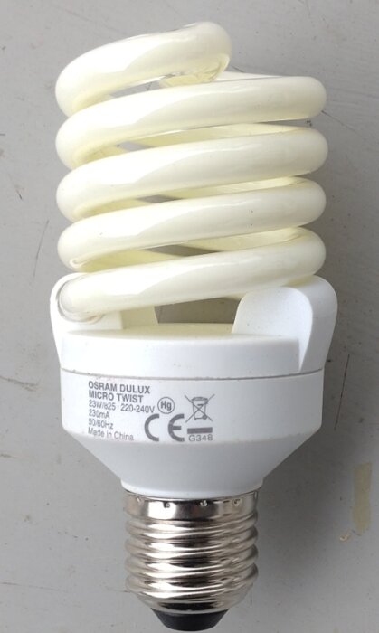 Compact lysrörslampa, Osram Dulux, spiralformad glödlampa liggande på en yta, text synlig på basen.