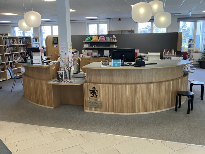 Reception i ett bibliotek med Staffanstorps kommunvapen monterat på en träpanel i ek, designad med olika fiberriktningar och dark ekfinish.
