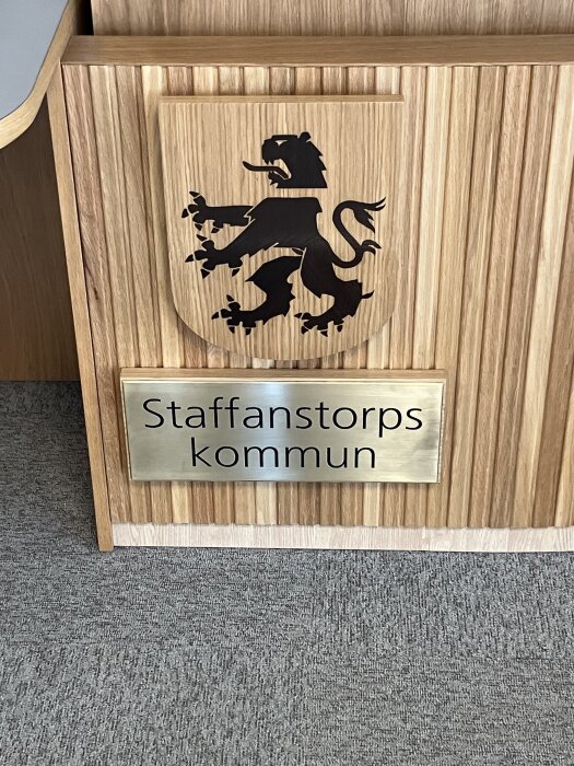 Staffanstorps kommunvapen i ek med skånsk grip, mörk kropp rökt med ammoniak, monterat i kommunhuset, trästrukturen har varierande fiberriktning.