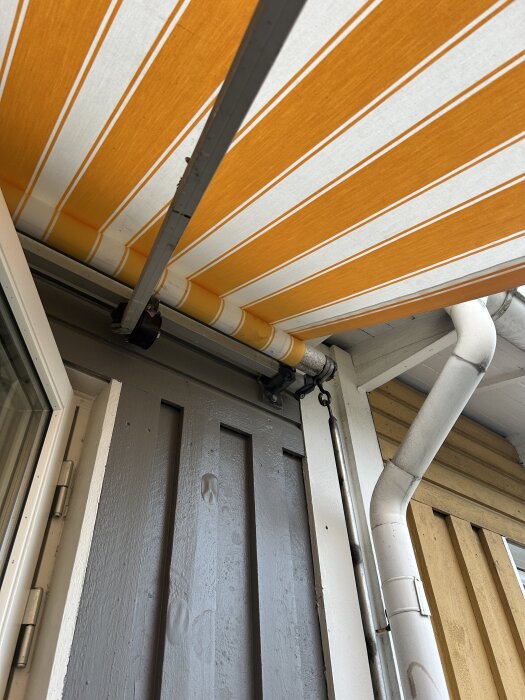 Randig markisduk i orange och vitt över en veranda med problem vid vevmekanismen.