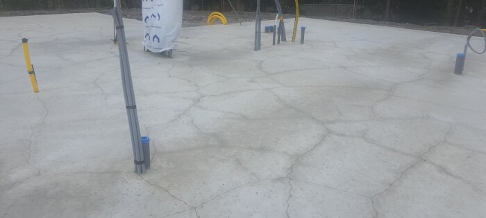 Betongplatta med sprickor och synliga genomföringar för byggprojekt. Sprickor tydliga över ytan.