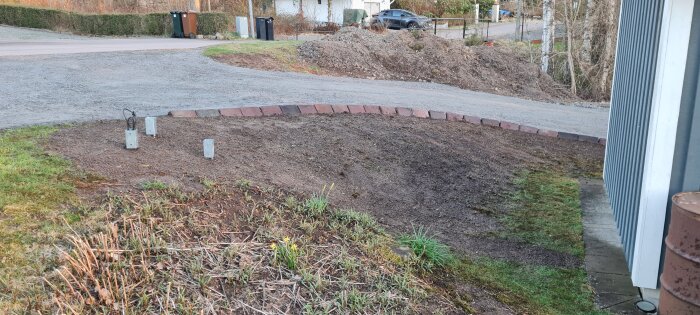 Tomt område i trädgården med återvunna kantstenar, grus och elektriska anslutningar nära friggeboden.