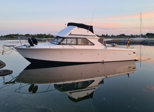En Bertram 28 Flybridge Cruiser som ligger förtöjd i ett lugnt vatten, reflekterad i ytan vid solnedgång.