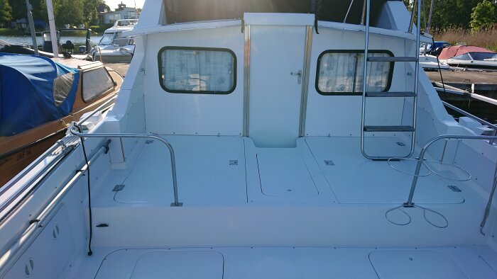 Akterdäck på Bertram 28 Flybridge Cruiser med teaktrappor, luckor på däck, metallräcken och förvaringsutrymmen i en småbåtshamn.