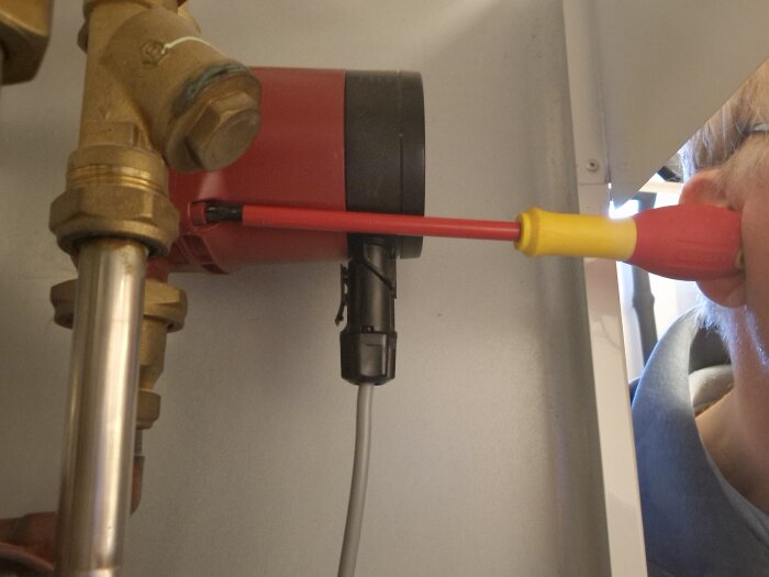 Person använder en skruvmejsel som stetoskop för att lyssna på en cirkulationspump i en fjärrvärmecentral.