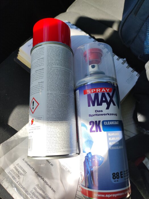 Sprayburkar med 2K klarlack från SprayMax och röd sprayfärg på en bänk.
