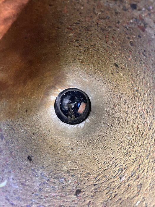 Insidan av en uppsamlingsbrunn med slamliknande material på väggarna. En inspektionslucka syns i botten av brunnen.