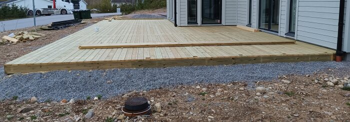 Nybyggd altan av trä invid ett hus. Grus och markeringar för landskapsarbete syns runt altanen.
