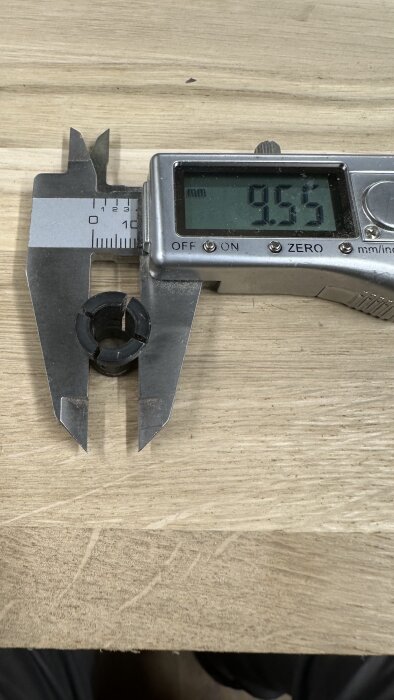 Digitalt skjutmått mäter diameter på svart hylsa till 9,55 mm på träunderlag.