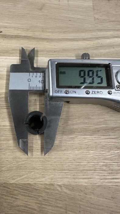 Digital skjutmått visar 9,95 mm diameter på en svart hylsa som mäts på ett trähörn.