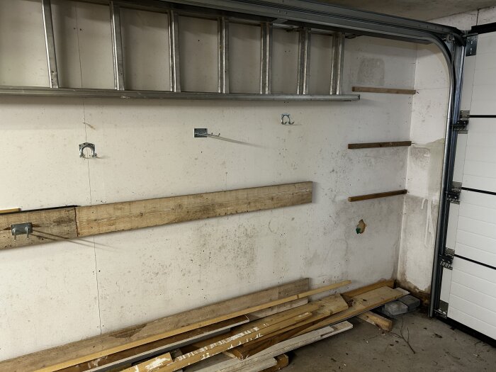 Friliggande garage med mögelskador på väggarna, visar hyllor, en stege och byggmaterial nedtill.