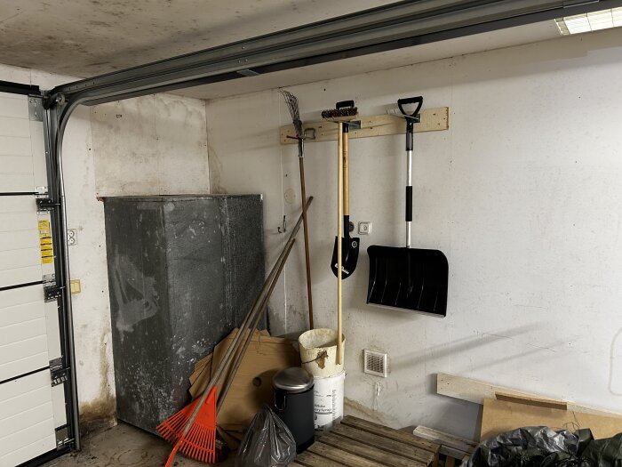 Garageinteriör med tecken på svartmögel på vägg och tak, verktyg som spade och kratta på väggen, och diverse förvarade föremål.