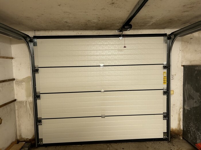 Garage med vita väggar, vit garageport, svartmögel synligt på tak och nedre delen av väggarna. Tecken på fuktskador och behov av renovering.