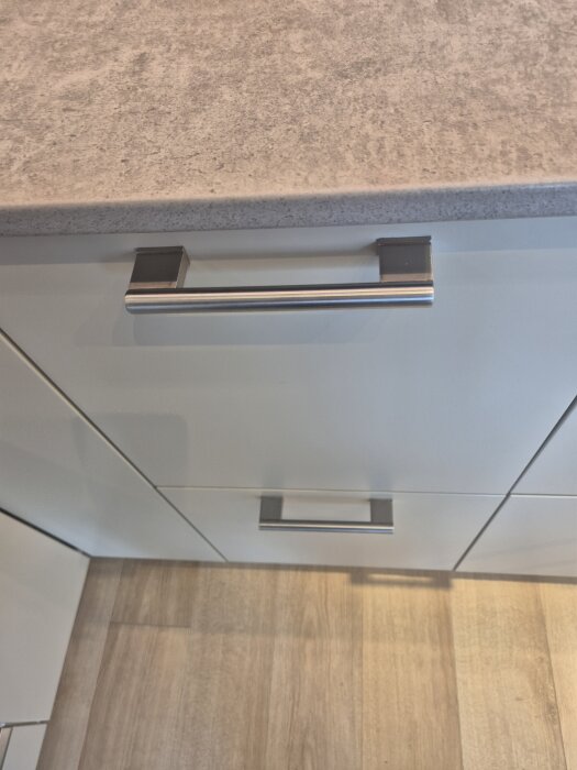 Köksskåpshandtag i metall på en låda under en grå köksbänk, sett i en köksutställning på Ikea.