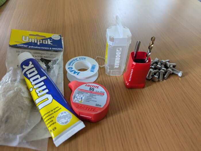 Verktyg och material för rörlagning inklusive Unipak packsalva, gängtejp, Loctite snör och Dormer borr- och gängsats på ett bord.