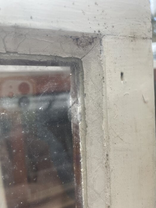 Närbild av ett gammalt fönster med sprucken färg och kitt runt glaset.