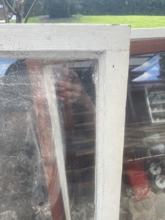 Närbild av ett fönster med glas monterat mot falsen och synligt kitt. Reflektioner och delar av omgivningen syns i glaset.