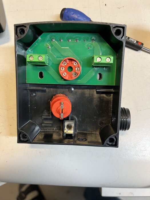 Inre del av en vridesomkopplare för pump med en grön kretskort och röd central del synlig ovanpå en verkstadsyta.