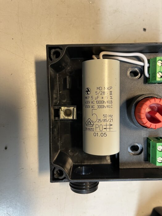 Kondensatoranslutning i en pump: vit kondensator märkt MD MKP, omgiven av kopplingsdetaljer i svart hölje, med gröna terminalblock och kablar.