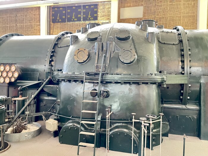 En äldre Jungströmsturbin i ett museum, med tillhörande mätare, ledningar och en trappa, från 1950-talet.