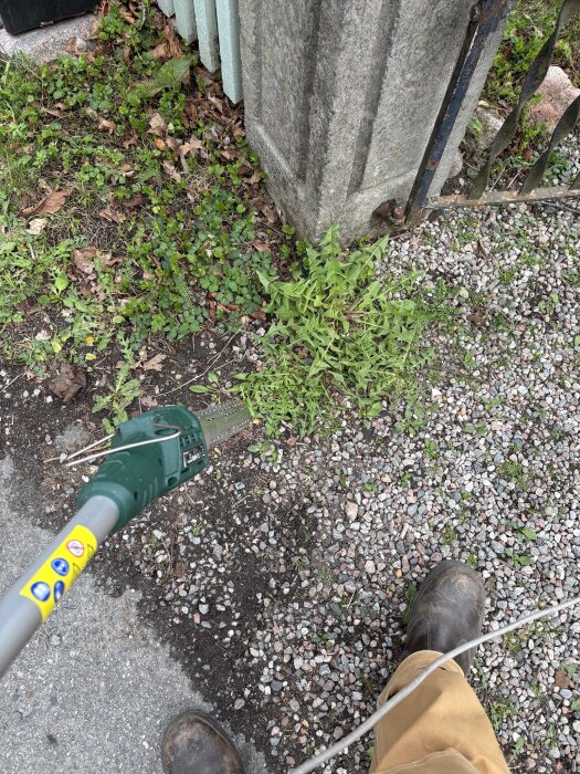 Rensning av ogräs vid staket med trimmer, fot synlig.