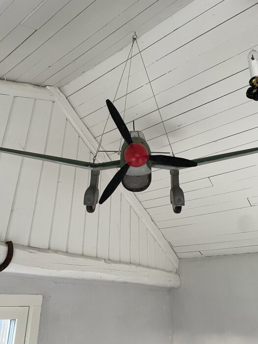 Modell av en Junker JU87 Stuka bombare hänger från taket i ett uterum, med propeller och landningställ synliga.