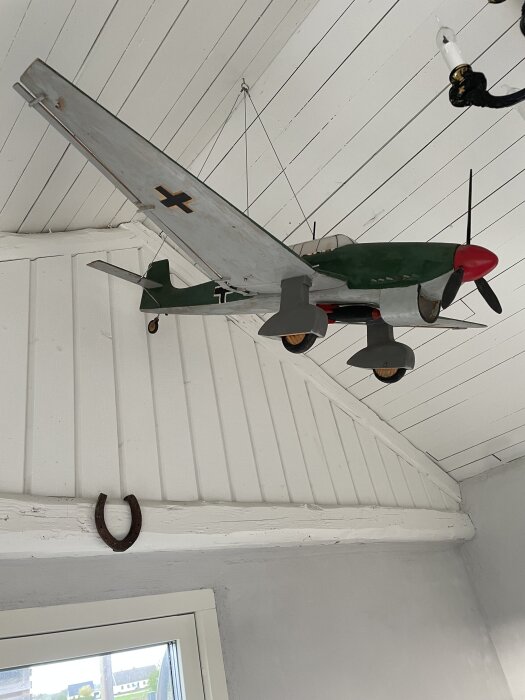 Modell av en Junker JU87 Stuka bombare hänger i ett uterum, med vitmålat trätak och en hästsko på väggen.