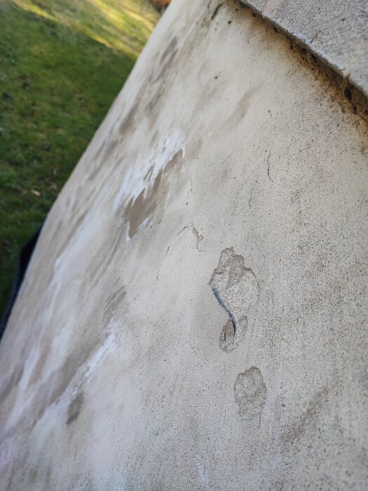 Vägg med saltkristaller och flagnande yta i dagsljus, potentiellt orsakat av saltutfällningar. Gräs i bakgrunden.