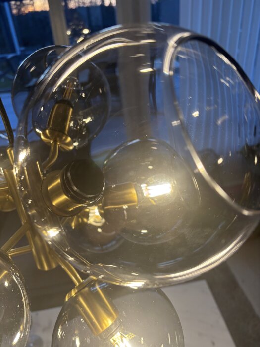 Glaskupa med lampsockel och snett fastskruvad låsring i plast, med synlig glödlampa och mässingsdetaljer.