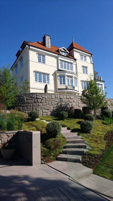 Ett stort hus med putsad fasad, murad med hydraliskt kalkbruk, omgiven av stensättning och grönskande trädgård.